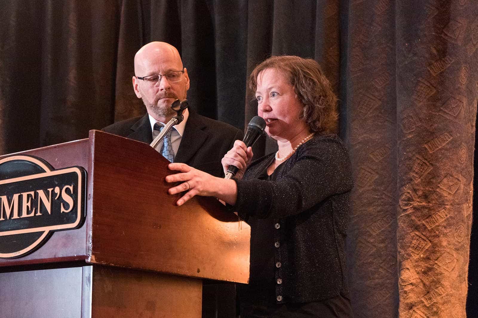 A man and woman stand on the stage behind a podium.