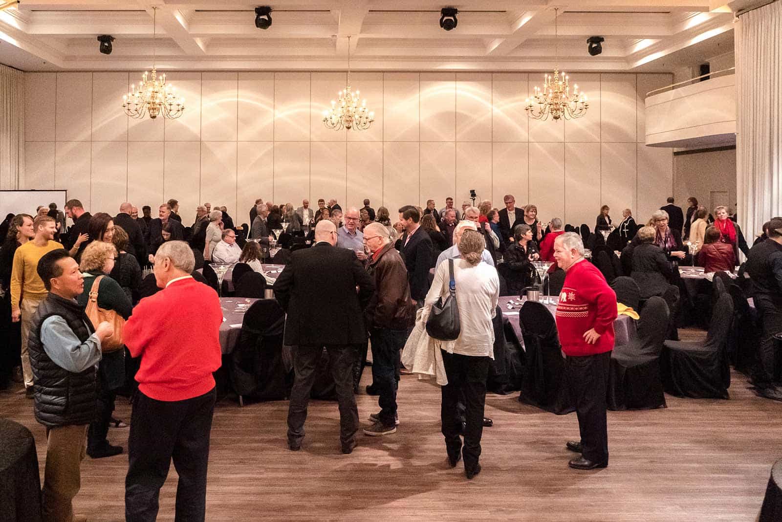 Over 225 guests milling around in discussion — a photo taken from the stage.