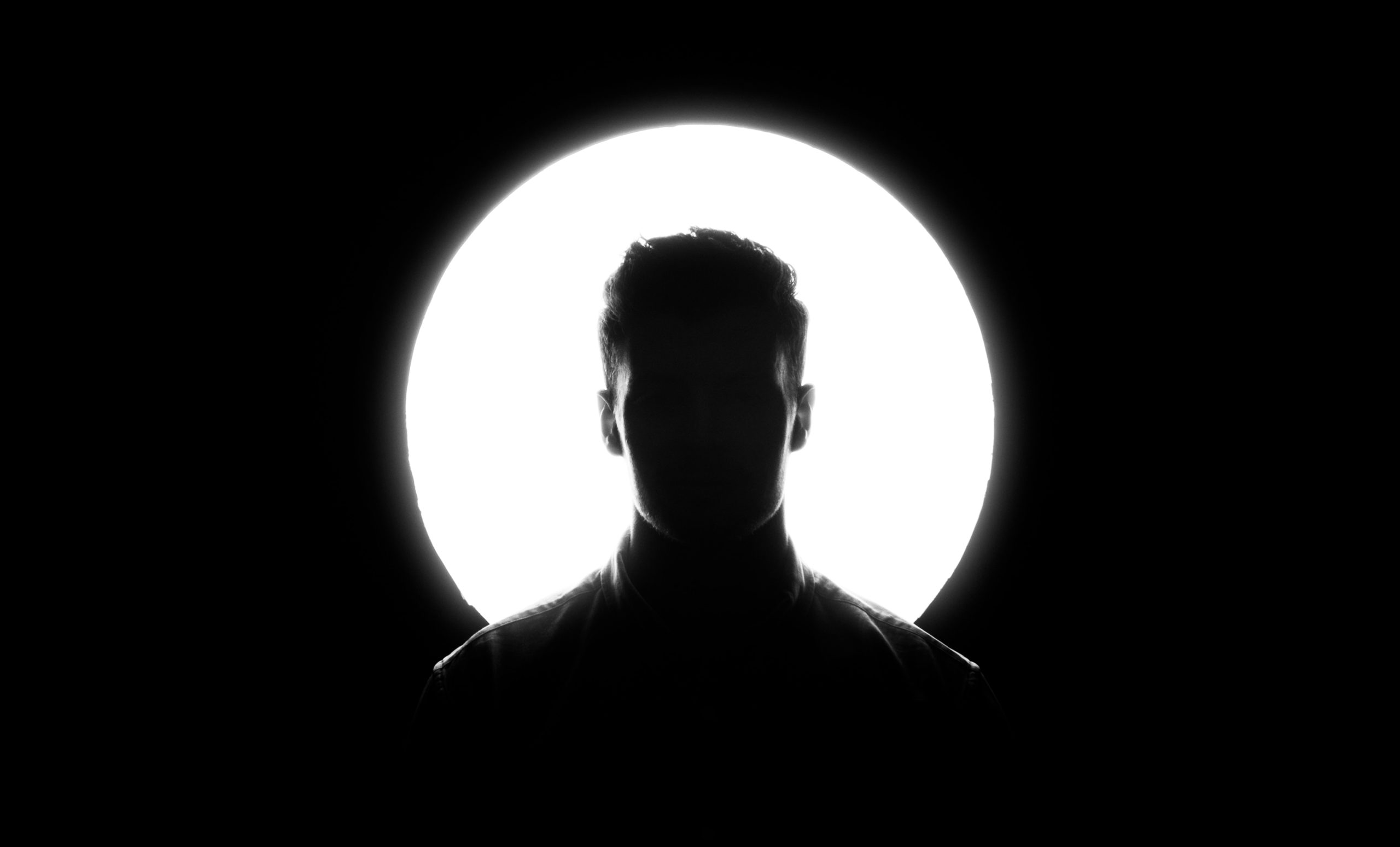 A silhouetted man stands against a backlight.